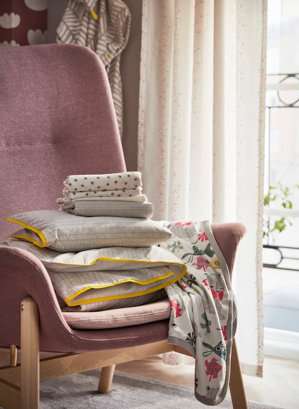 Fauteuil VEDBO en rose pâle avec une pile de linge de lit pour bébé