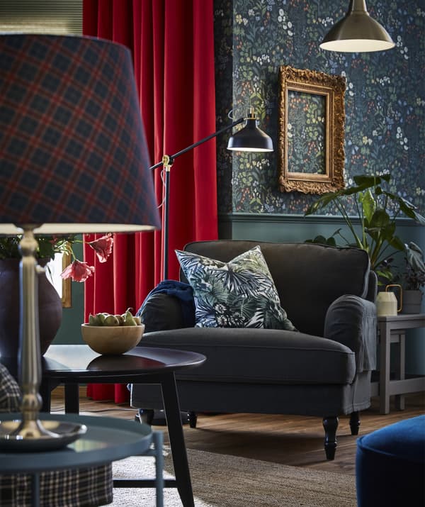 Fauteuil vert foncé garni d’un coussin à motif floral, avec à l’avant-plan une lampe décorée d’un abat-jour motif tartan posée sur une table d’appoint.