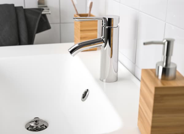 Close-up of a white sink with a chrome plated faucet, with a bamboo soap dispenser.