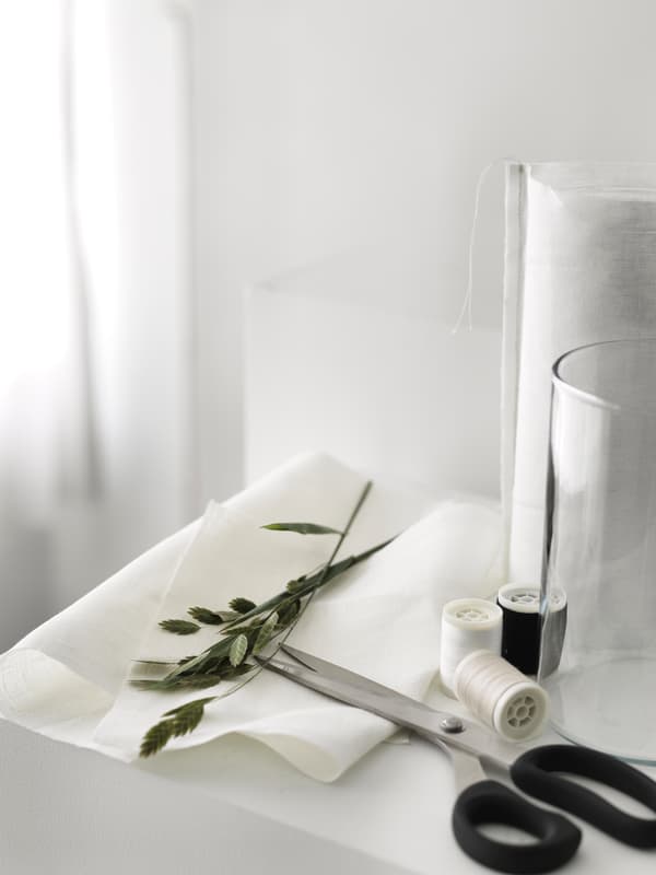 Fehér anyag, olló, cérnák és zöld növény előkészítve a váza díszítéséhez.