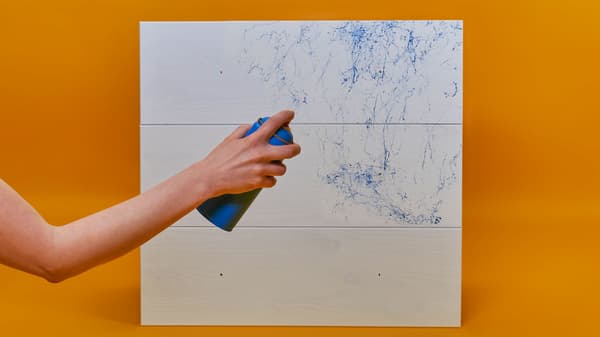 Fehér fiókelőlapokra kék márványhatású festéket fúj egy kéz.