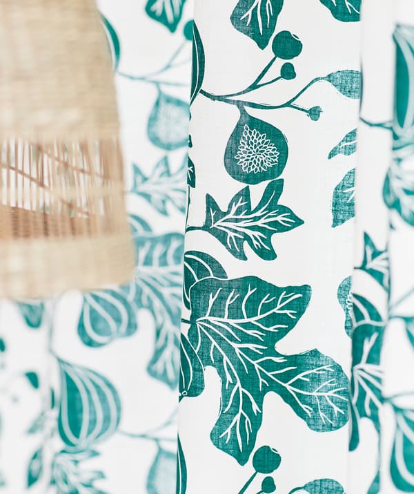 Fehér függöny zöld fügeág mintával egy banánrostból készült mennyezeti lámpa mellett.