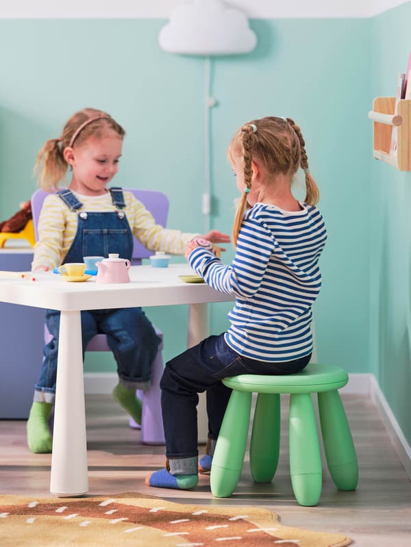 Fehér MAMMUT asztal mellett két lány, egyikük zöld MAMMUT ülőkén, a másik lila MAMMUT gyerekszéken ül. 