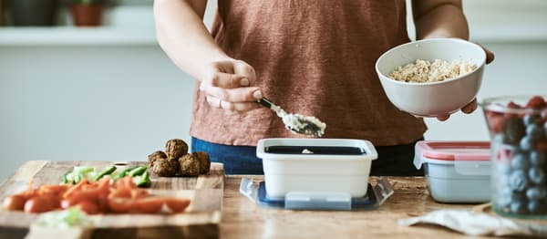  Fehér műanyag élelmiszer dobozok tetőkkel az asztalon, zöldséggolyók és szeletelt zöldségek a bal oldalon.