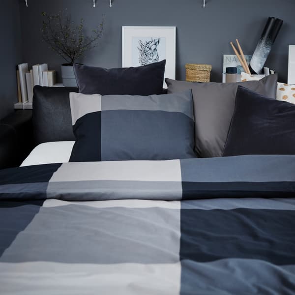 Fekete bőr kanapé, fekete/szürke ágyneművel és szürke, fehér / arany és sötétszürke bársony pamut párnákkal.