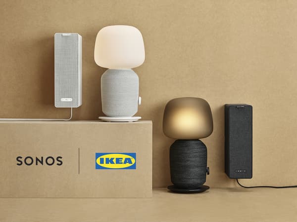 Fekete és fehér SYMFONISK asztali lámpák, beépített WiFi hangszórókkal és két függőlegesen felakasztott könyvespolc hangszóró a Sonostól és az IKEA-tól.
