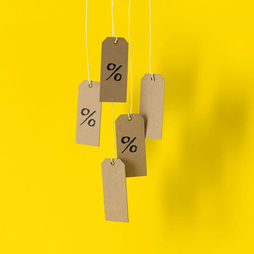 Fem bruna prisettiketer med % tecken hänger mot en gul bakgrund i snören från taket.