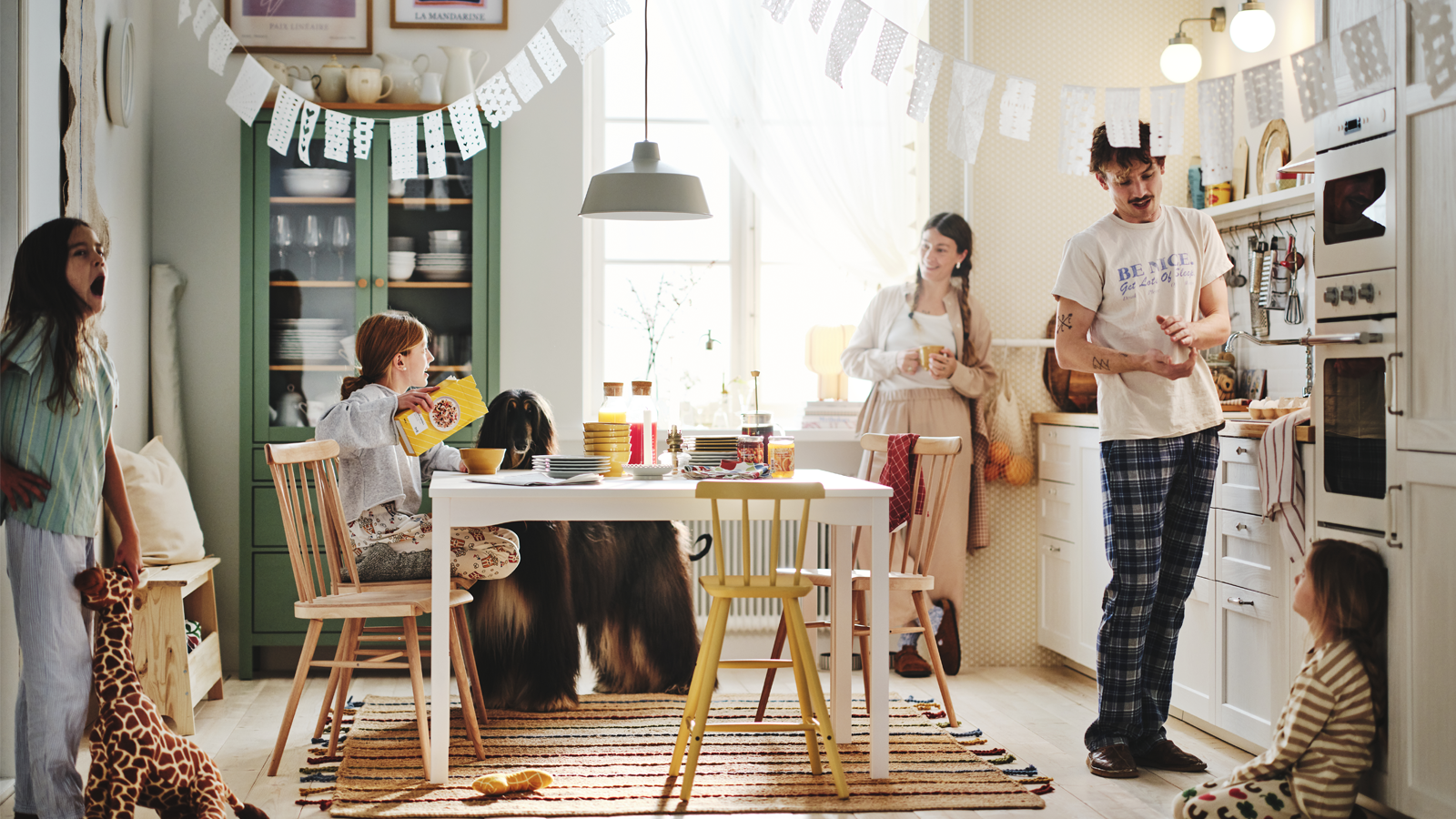 Fem personer og en hund er samlet i et hyggeligt køkken 