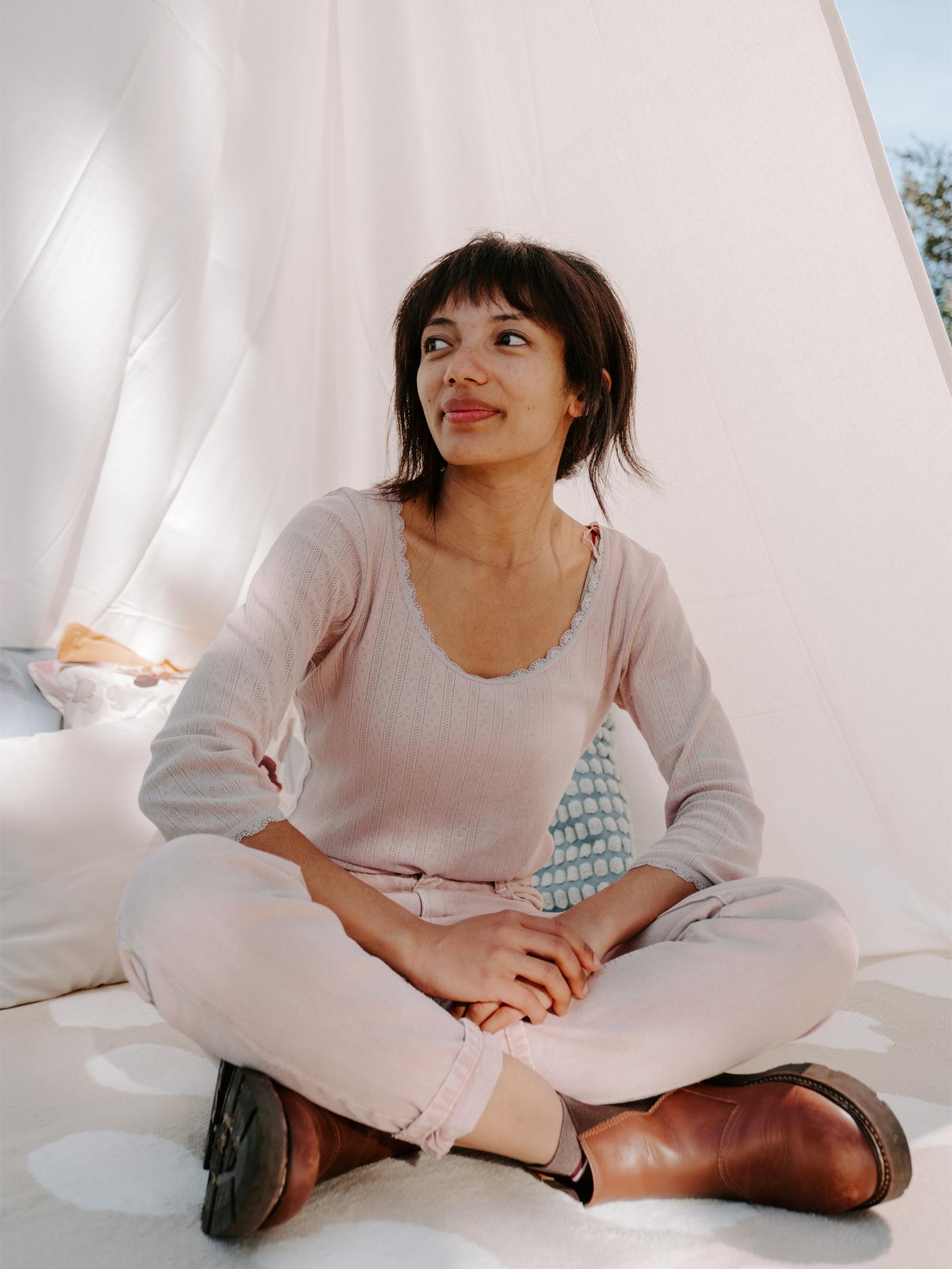 Femme assise les jambes croisées par terre à l'intérieur d'une tente blanche