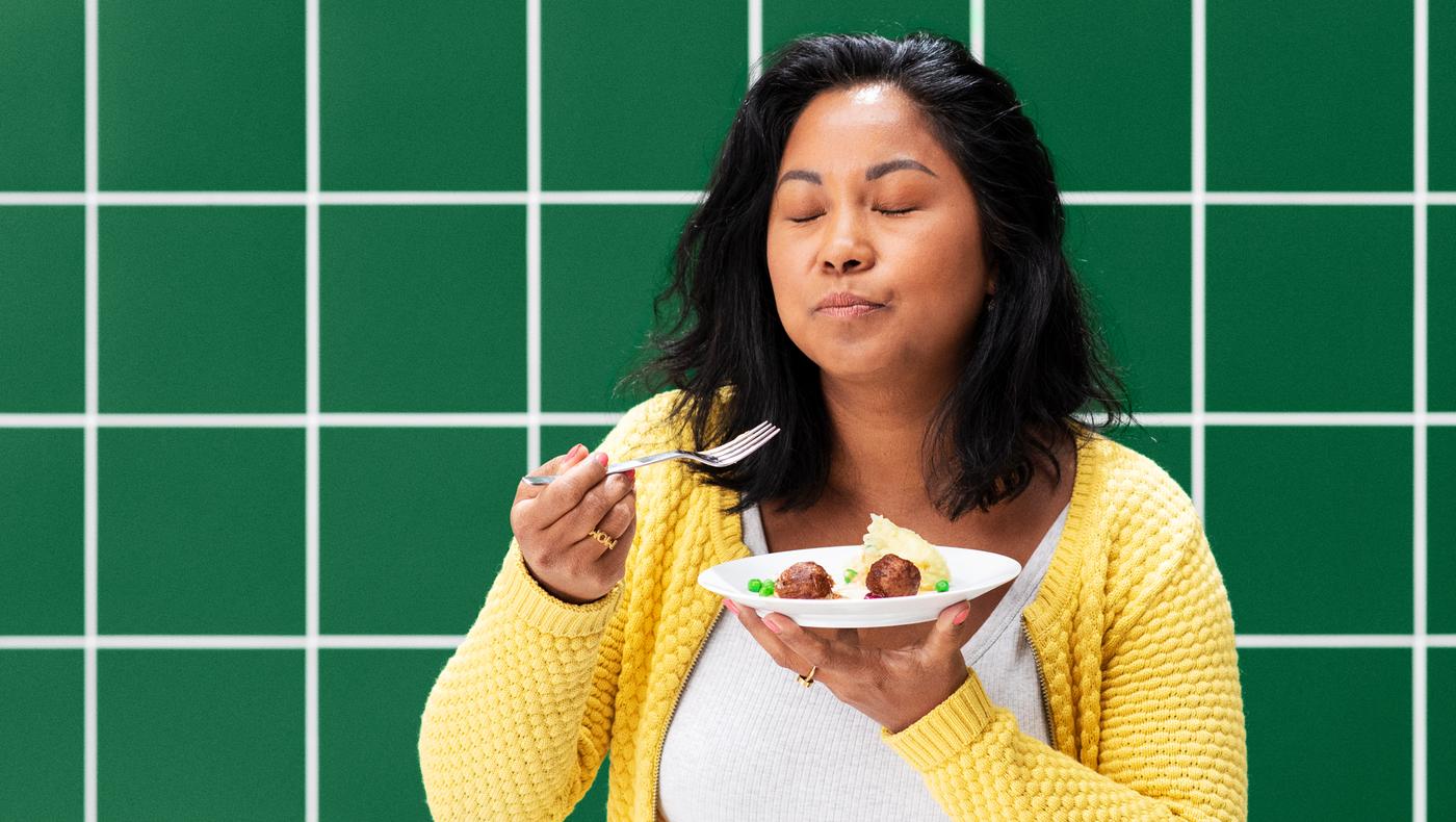 Femme aux yeux fermés tenant dans sa main une assiette de savoureuses boulettes végétales agrémentées d’un écrasé de pommes de terre et de petits pois.