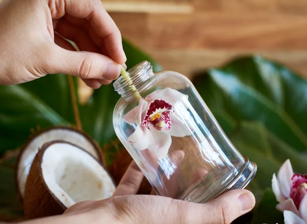 Femme en train de glisser une fleur d’orchidée dans un flacon en verre.