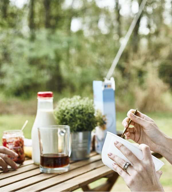 Femme en train de tenir en main un bol petit déjeuner à une table, à l’extérieur.