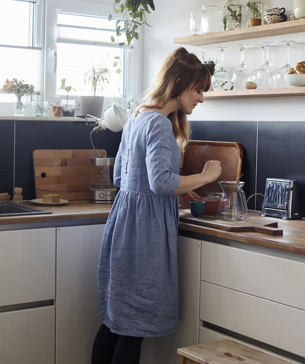 Femme préparant du thé dans le coin d’une cuisine bleue et blanche.
