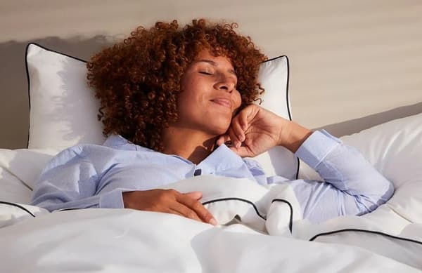 Femme qui dort allongée sur le dos dans son lit en pyjama bleu