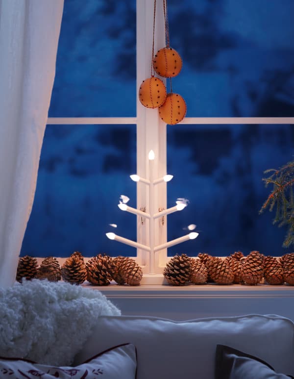 Fenêtre décorée d'une guirlande lumineuse disposée en zigzag et d'un petit cheval en bois suédois.