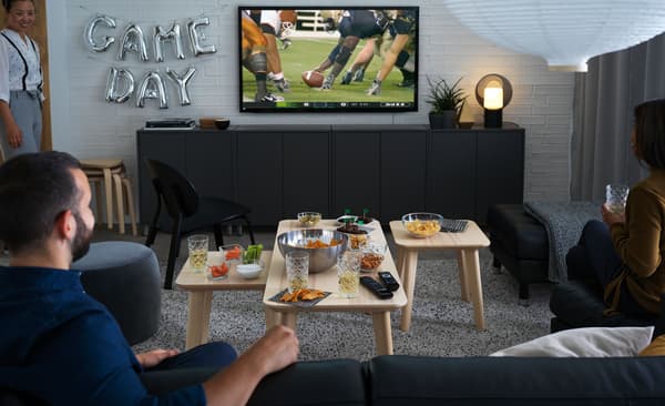 Férfi és nő ülnek egy kanapén, sport műsort néznek a TV-ben, miközben nassolnak.