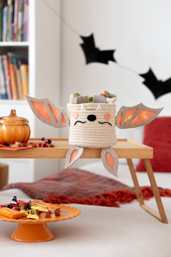 Fertiges DIY Halloweenkörbchen steht auf einem Tablett. Halloweendekoration liegt daneben.  