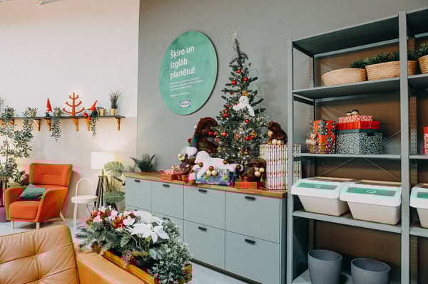 Festive IKEA corner with a decorated Christmas tree, wrapped gifts, plush toys, and recycling bins on shelving.