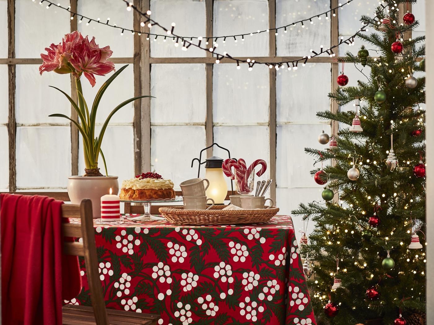 Festlich dekorierter Essbereich mit weihnachtlicher IKEA-Tischdecke in Rot mit Beerenmuster, gedecktem Tisch, Lichterketten und geschmücktem Weihnachtsbaum – stimmungsvolle IKEA-Weihnachtsdeko für ein gemütliches Zuhause