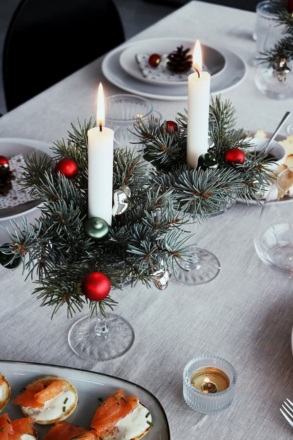 Festliche Tischdekoration mit brennenden Kerzen in grünen Kränzen, roten und grünen Ornamenten und Tellern mit Vorspeisen. Gemütliche Weihnachtsstimmung.