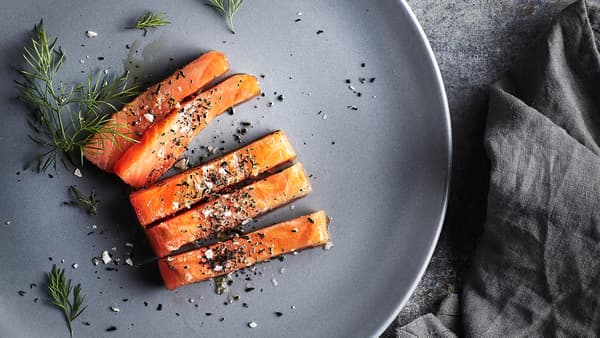 Filets de salmó amb una mica de sal, pebre i anet a un plat gris. Al costat del plat hi ha un tovalló gris.
