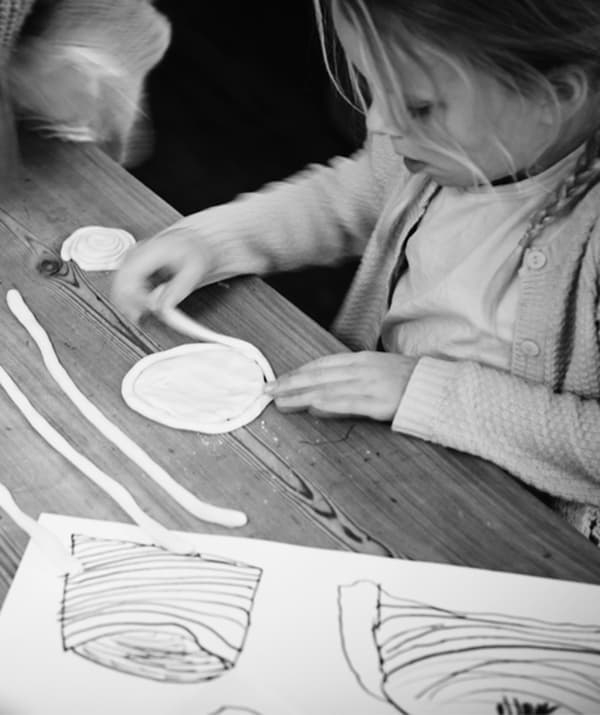 Fillette debout près d’une table, enroulant de minces boudins de pâte pour former des disques prêts à aller au four.