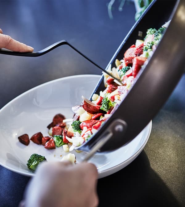 Finished sausage and veggies being poured into a serving bowl