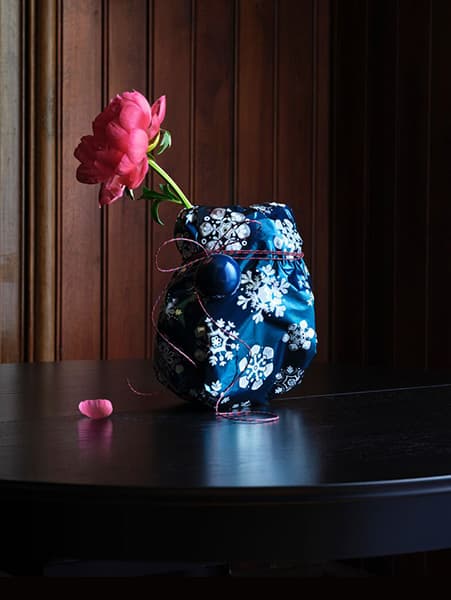 Fiore artificiale all'interno di un vaso coperto da un tessuto e su un tavolo nero.
