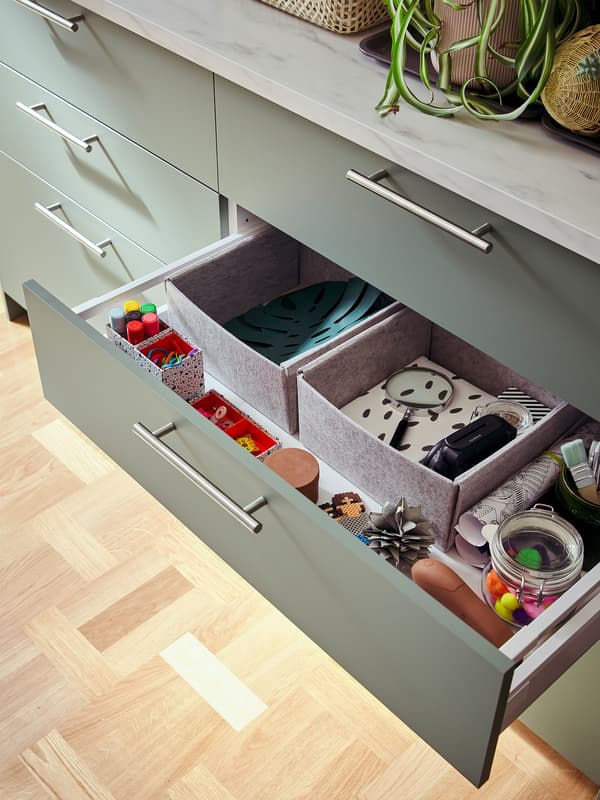 Five drawers in grey green below a light-grey mineral effect worktop. One drawer is open showing boxes, pens and more.