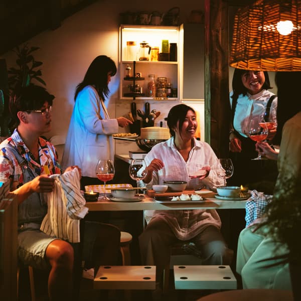 Five people around a set of 4 black/birch effect FRIDNÄS nesting tables with stools below a KAPPELAND pendant lamp shade.