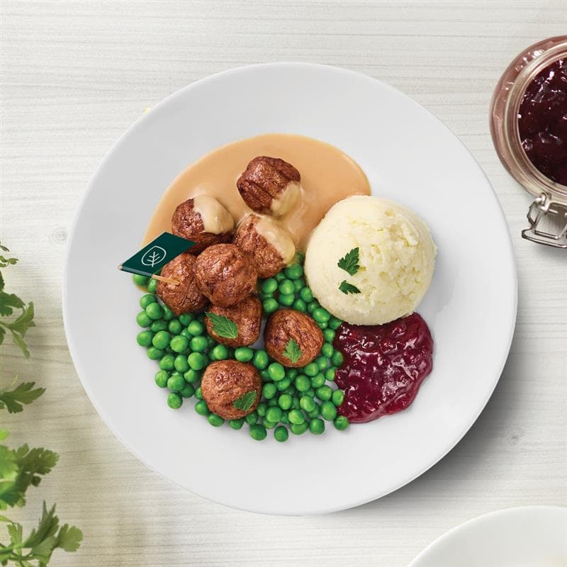 Fleisch(los)bällchen mit Kartoffelpüree, Erbsen und Preiselbeeren auf einem Teller präsentiert.