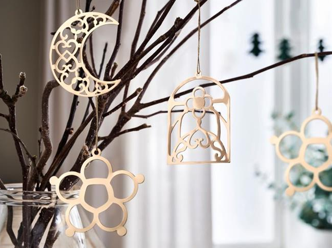 Flera GOKVÄLLÅ dekorationer hänger i trägrenar som står i en glasvas vid ett fönster. 