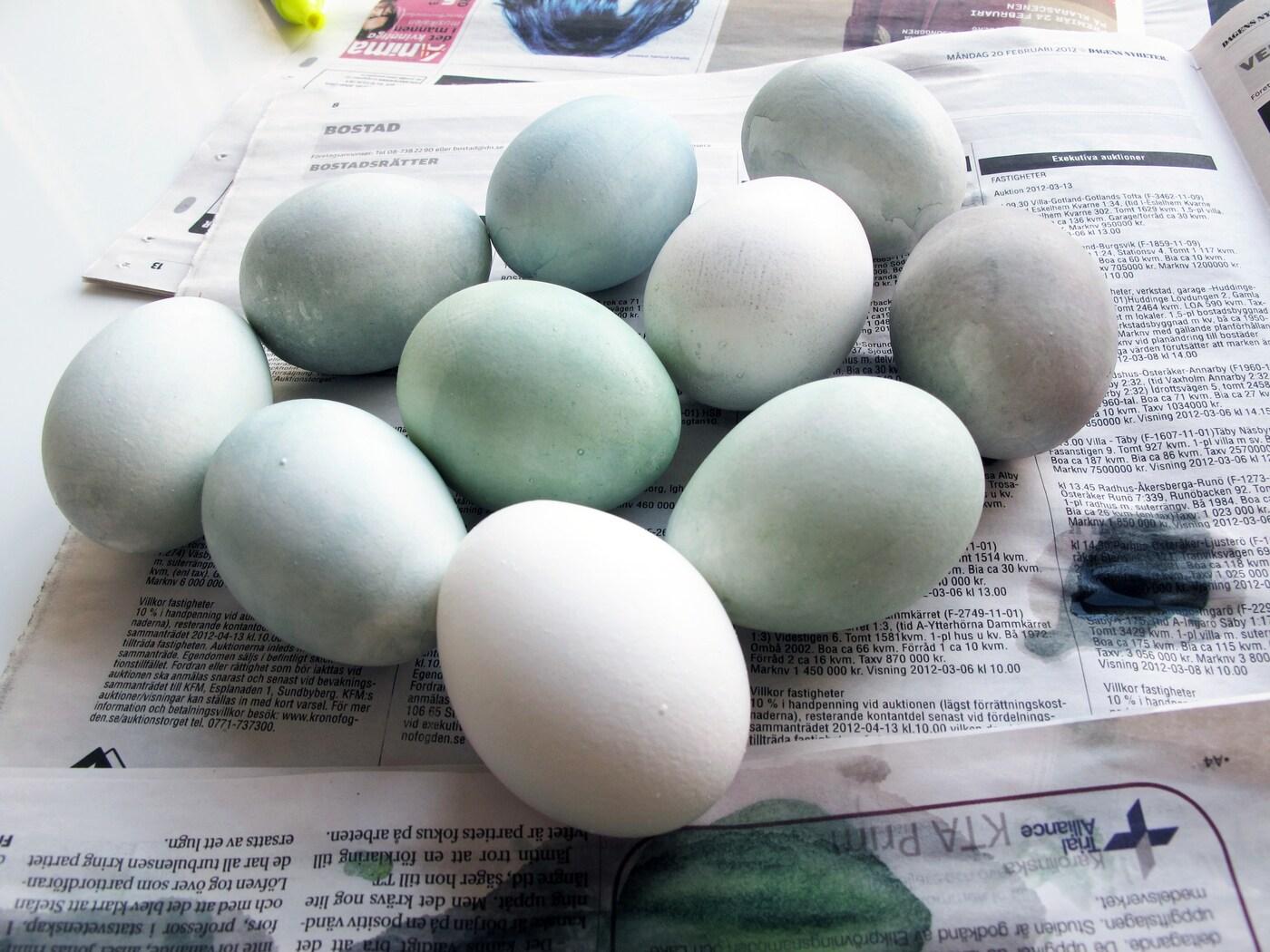 Flera nyfärgade ägg utav vattenfärg ligger på tork på tidningspapper. 