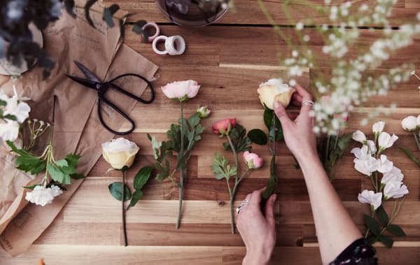 Fleurs artificielles et naturelles, ciseaux et rouleaux de ruban adhésif sur une table en bois.