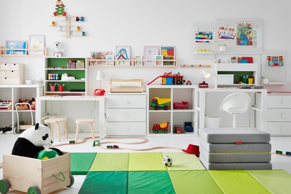 ห้องเด็กที่มีของเล่นอยู่บนพื้น โต๊ะอยู่ด้านข้าง รวมทั้งภาพวาดบนแผ่นเส้นใยไม้อัดและที่วางรูปภาพ FLISAT/ฟลิแซท บนผนัง