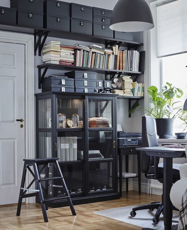 Floor-to-ceiling storage solution in a home office. A black ladder gives access to the highest shelves.