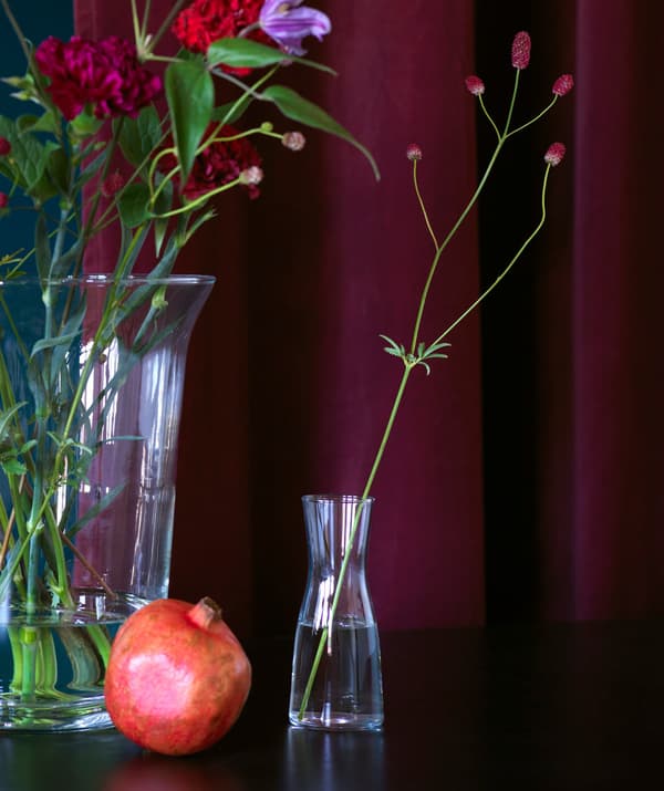 Floreiros de cristal con arranxos florais sinxelos diante dunha cortina en vermello intenso.