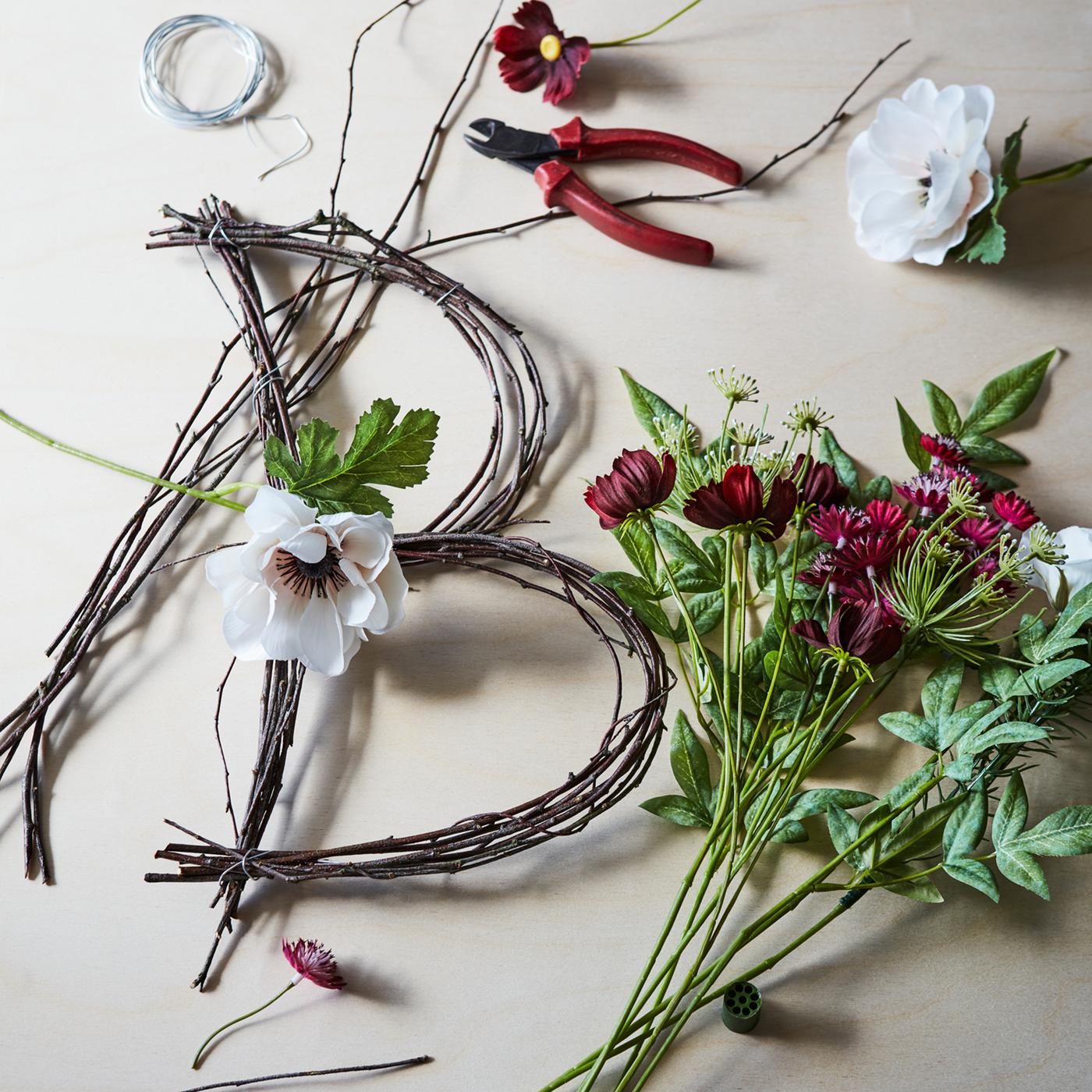 Flowers and twigs in the process of being made into a letter B floral decoration lying on a surface with a pair of pliers.