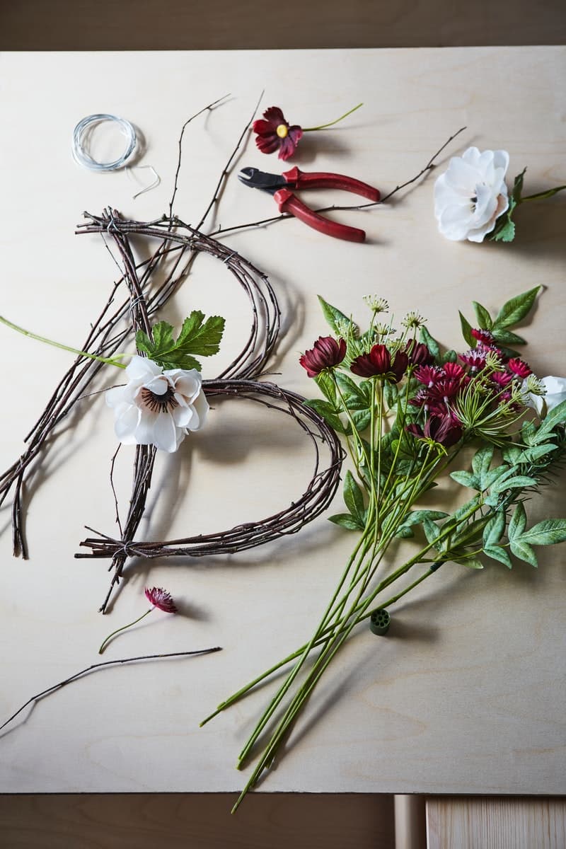 Flowers and twigs in the process of being made into a letter B floral decoration lying on a surface with a pair of pliers.