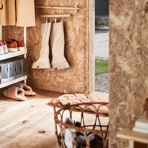 Flur mit einer weißen Garderobe mit Schuhaufbewahrung, einem SNIDAD Korb mit Schuhen und Wandstangen mit Stiefeln an Bügeln.