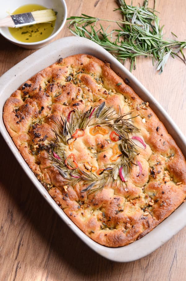 Focaccia appena sfornata con erbe e olio d'oliva su un tavolo di legno.