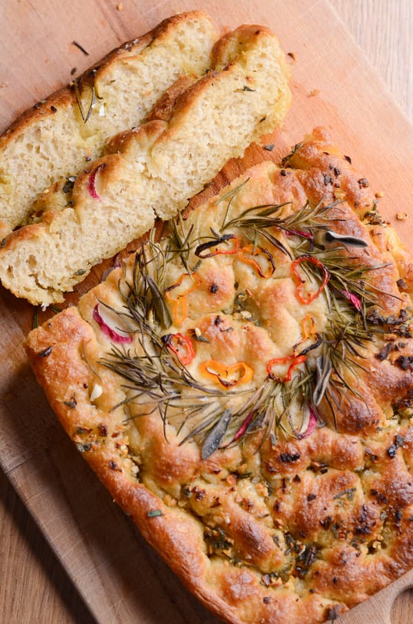 Focaccia con erbe e peperoncino a fette su una tavola di legno, con un pezzo tagliato e posizionato sopra.