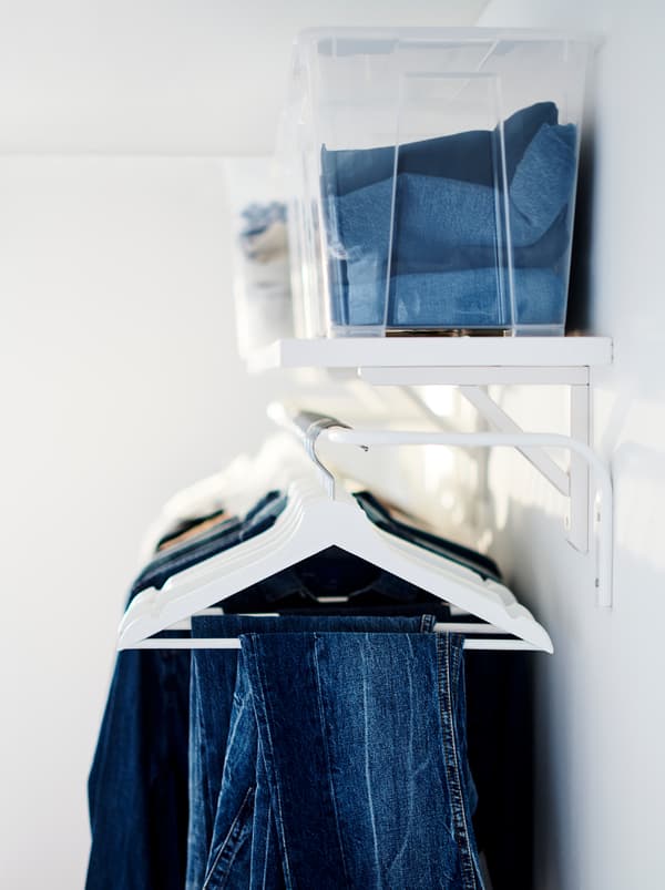 Folded clothes in transparent boxes and a BERGSHULT shelf. Below it hang a row of clothes on BUMERANG hangers.