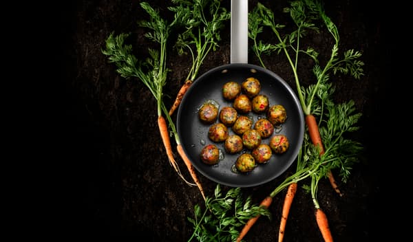 Fons negre en què es veu una paella envoltada de pastanagues i, a dins, mandonguilles vegetarianes