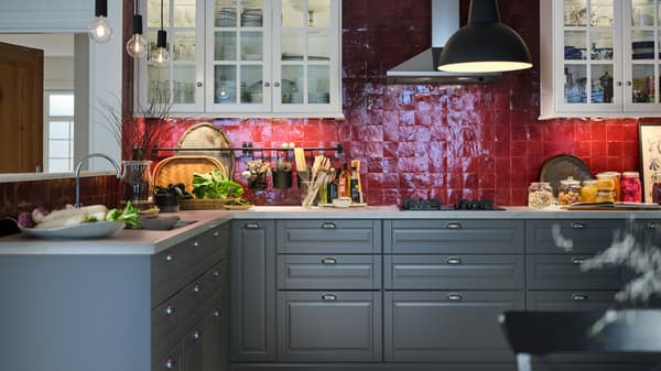 Food and accessories in a red-tiled kitchen with white wall cabinets, grey base cabinets and a white marble effect worktop.