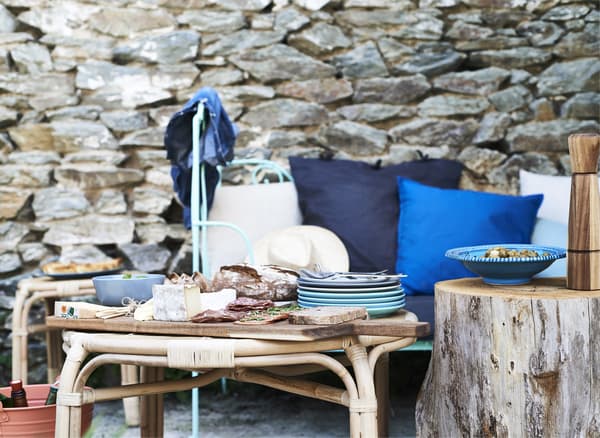 Food served on wooden boards on a coffee table and a seat with blue cushions against an old brick wall.