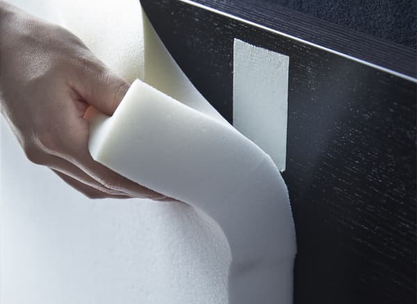 For a DIY padded headboard, you can cut foam panels and use double-stick tape to attach them to the headboard. We put them on a black-brown MALM bed frame and then covered it with a velvet curtain and some thread.