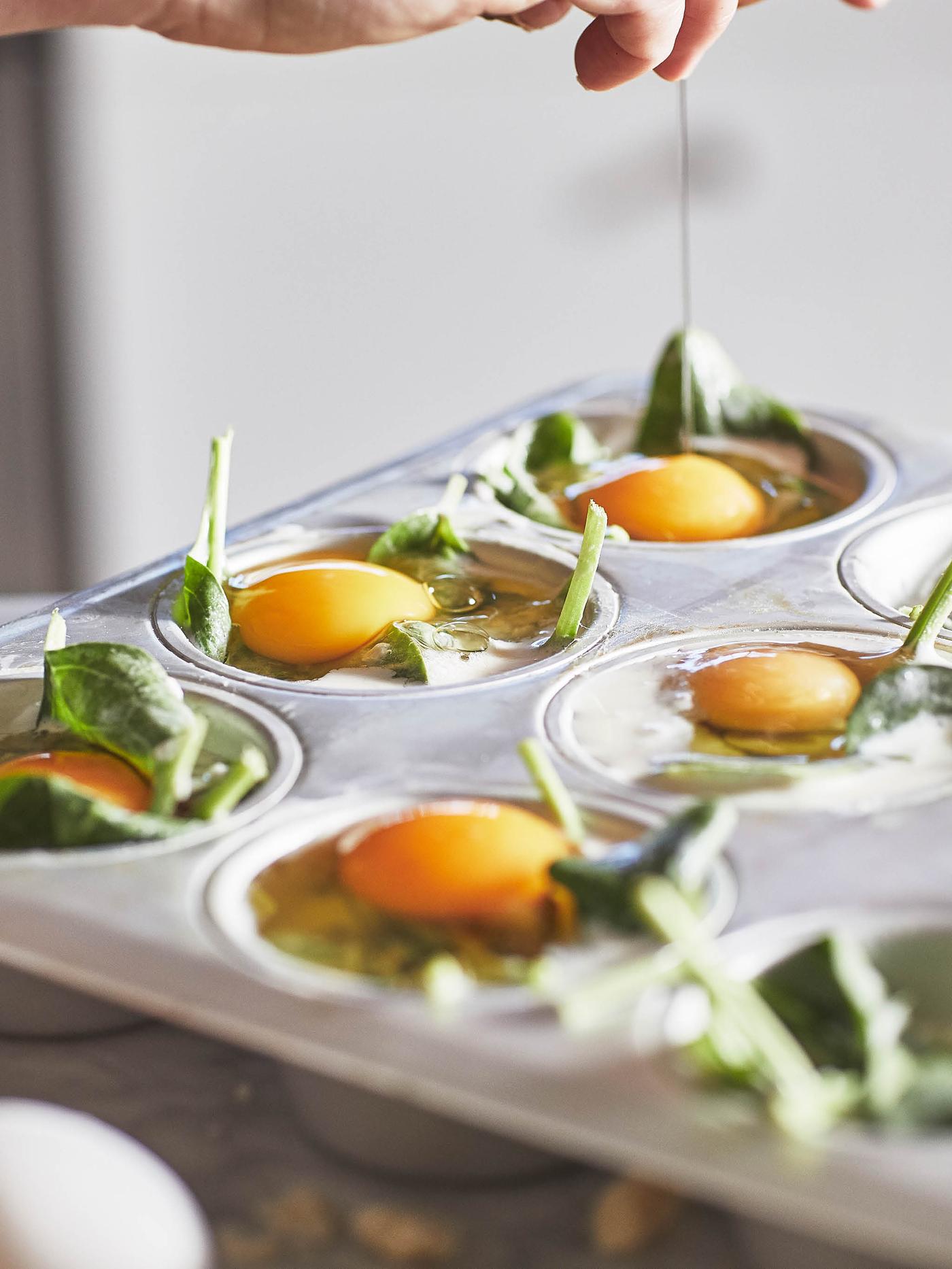 Forma na muffiny VARDAGEN plná porcí špenátu s těstem a syrovým vejcem.