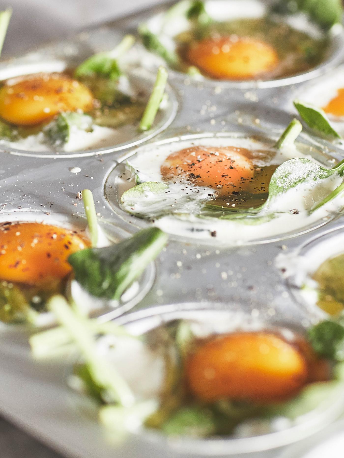 Forma na muffiny VARDAGEN plná porcí špenátu s těstem, syrovým vejcem a kořením.