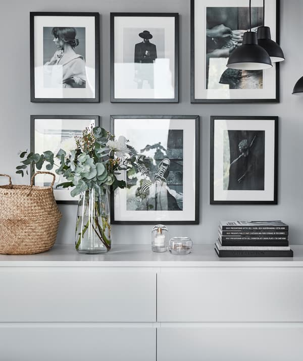 Foto in bianco e nero incorniciate appese sopra due cassettiere bianche.